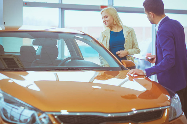 Concessionnaire avec femme se tient près d'une nouvelle voiture dans le showroom - Photo, image