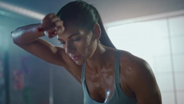 Close Up Portrait of a Beautiful Strong Fit Brunette Wiping Sweat from Her Face in a Loft Industrial Gym with Motivational Posters. She's Catching Her Breath after Intense Fitness Training Workout. - Filmagem, Vídeo