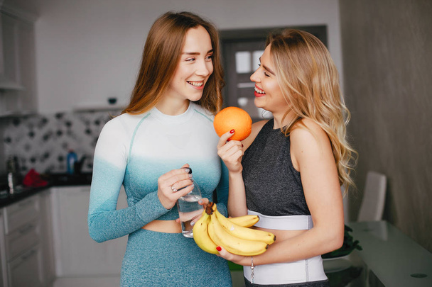 Two sports girl in a kitchen with vegetables - Foto, afbeelding