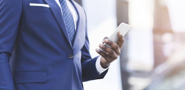 Hombre de negocios afroamericano enviando mensajes de texto a través de teléfonos inteligentes caminando en el área urbana
 - Foto, Imagen