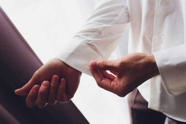 The man fastens the cuffs of the shirt. Morning of the groom. Hands of wedding groom buttoning up his white shirt. Males hands on a background of a white shirt, sleeve shirt with cufflinks. Close-up. - Fotoğraf, Görsel