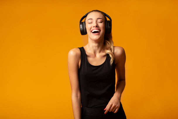 Sportowa dziewczyna w słuchawkach bezprzewodowych słuchanie muzyki, żółte tło - Zdjęcie, obraz