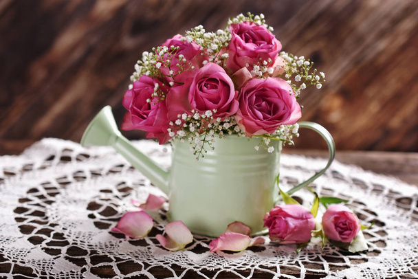 bunch of pink roses in a watering can on wooden table - Fotoğraf, Görsel
