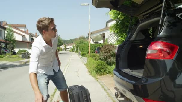 CERRAR: Emocionado joven lanza su equipaje en la parte posterior de su gran SUV negro. Viajero feliz viviendo en los soleados suburbios lanzando bolsas de viaje en su coche antes de emprender un divertido viaje por carretera
. - Metraje, vídeo