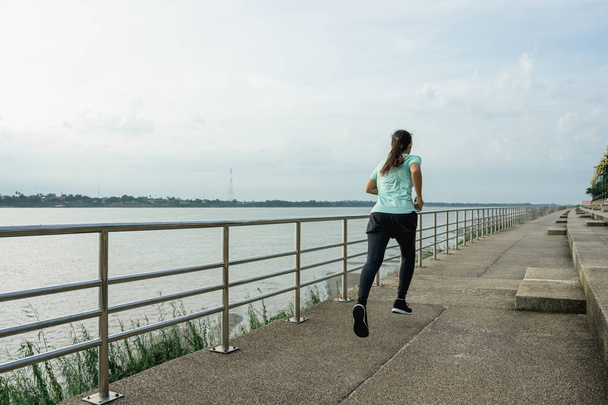 Young woman running on the street with a view of the river in the morning. - Fotó, kép
