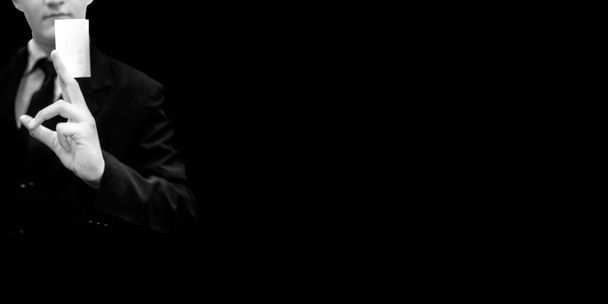 Бизнесмен в темном костюме с черным галстуком на черном фоне с визитной карточкой или белой карточкой в стильной манере, идеально подходящей для рекламы
. - Фото, изображение