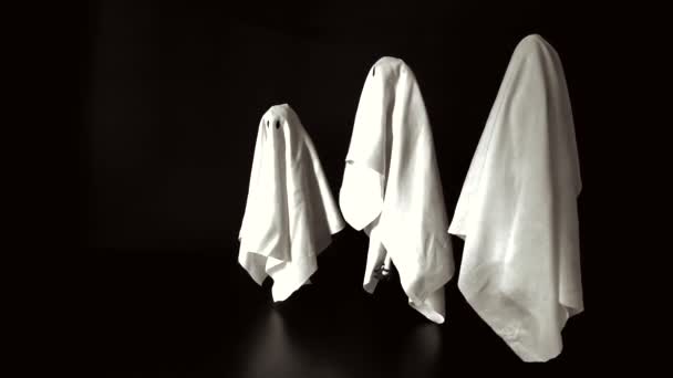 Filma un grupo de trajes femeninos de sábanas blancas fantasmas volando en el aire con fondo negro. Mínimo concepto de miedo de Halloween
. - Metraje, vídeo