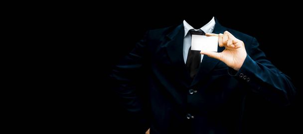 Unrecognizable faceless gentleman or seller holding white colored card in his hand wearing a dark blue colored suit with black necktie isolated on black.Concept of marketting. - Фото, зображення
