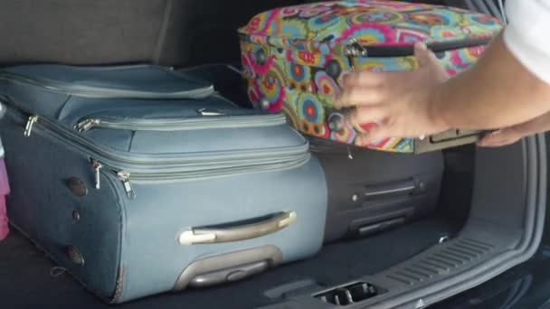 Lassított, közelről: felismerhetetlen férfi turista csomagolás ő és barátnője táskák a hátán egy tágas fekete autó. Ismeretlen ember üzembe poggyász fekete autót parkolt a napfényes úttestről. - Felvétel, videó
