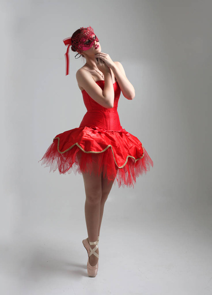 赤いバレリーナチュチュとマスクを着けている女の子のフルレングスの肖像画。スタジオの背景に対してダンスポーズ. - 写真・画像