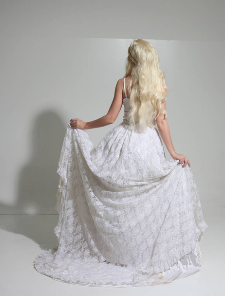 retrato de comprimento total da menina loira vestindo longo vestido de noiva de renda branca. pose de pé em um fundo de estúdio
. - Foto, Imagem