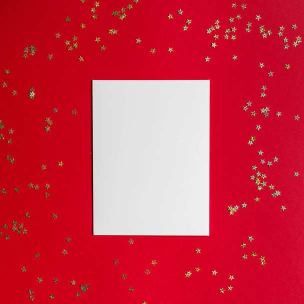 Christmas composition. White blank paper on red background with golden confetti. Winter holidays, new year concept. Greeting card, xmas celebration 2020. Flat lay, top view, copy space, mockup - Φωτογραφία, εικόνα