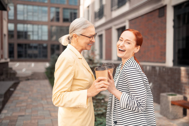 Счастливые деловые женщины. Талия двух довольных деловых леди в модной одежде, смеющихся на улице перед офисным зданием
 - Фото, изображение
