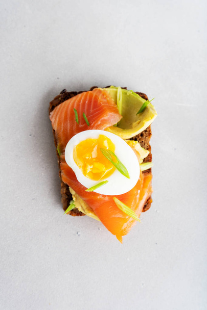 Top view of sandwich on rye toast with avocado, salmon, egg and spring onion on white plate background - Foto, immagini