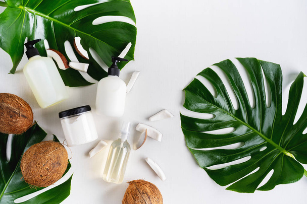 Cosmetic set of bottles for packaging on grey concrete background with green leaves and coconuts  - Foto, afbeelding