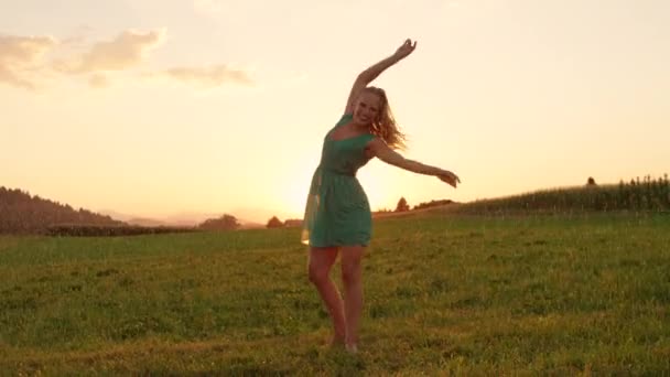 FLARE DE LA LENTE, ESPACIO DE COPIA: Feliz joven bailarina que gira al aire libre en una agradable noche lluviosa. Pintoresca naturaleza veraniega y dorada salida del sol rodean a una rubia despreocupada bailando sola bajo la lluvia
. - Metraje, vídeo