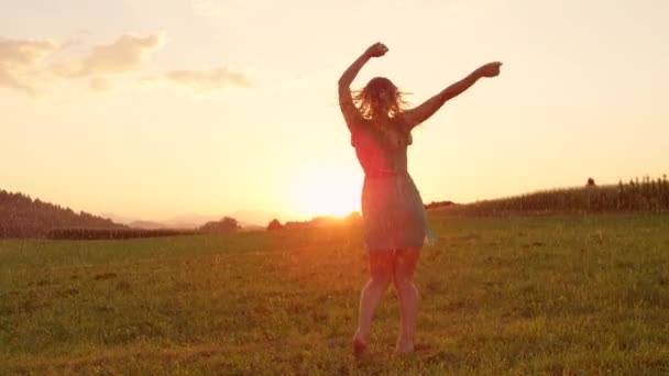 SLOW MOTION, LENS FLARE, COPY SPACE: Pretty Caucasian woman twirls elegantly in a cool spring shower at sunset. Stunning shot of happy blonde girl dancing in the morning in beautiful summer nature. - Video