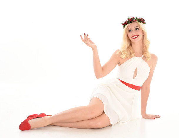 полноразмерный портрет блондинки в белом платье и цветочной короне. Сидящая поза, изолированная на белом фоне студии
. - Фото, изображение