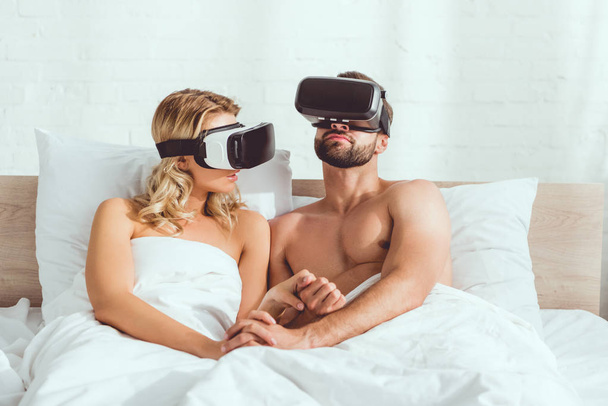 jovem casal deitado na cama ao usar fones de ouvido realidade virtual
  - Foto, Imagem