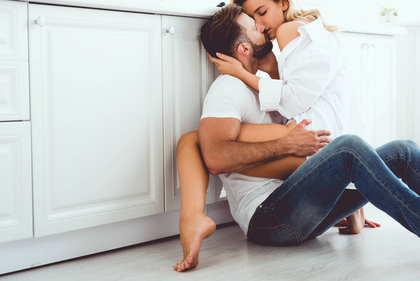 young couple hugging and kissing while sitting on floor in kitchen - Fotoğraf, Görsel