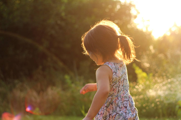 sylwetka małej dziewczynki z kucyk w sukni kwiatowych na zewnątrz w promieniach słonecznego zachodu słońca - Zdjęcie, obraz