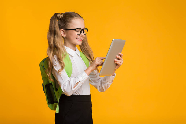 Smiling Elementary School Girl Using Digital Tablet Over Yellow Background - Foto, immagini