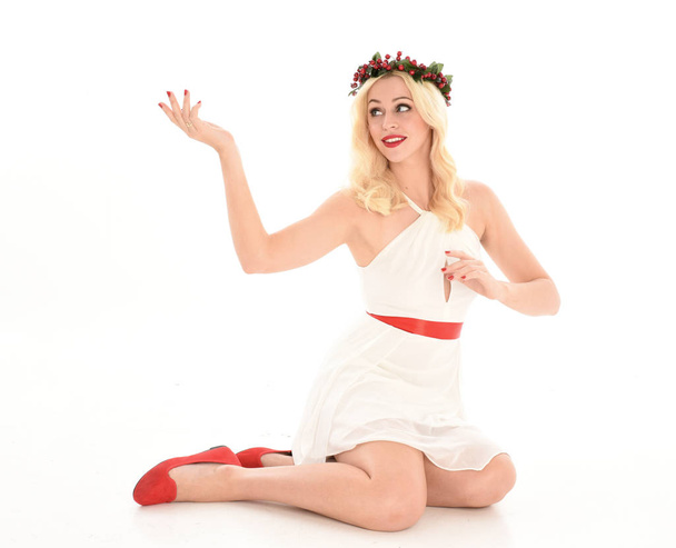 retrato de comprimento total da menina loira vestindo um vestido branco e coroa de flores. Sentado pose, isolado contra um fundo de estúdio branco
. - Foto, Imagem