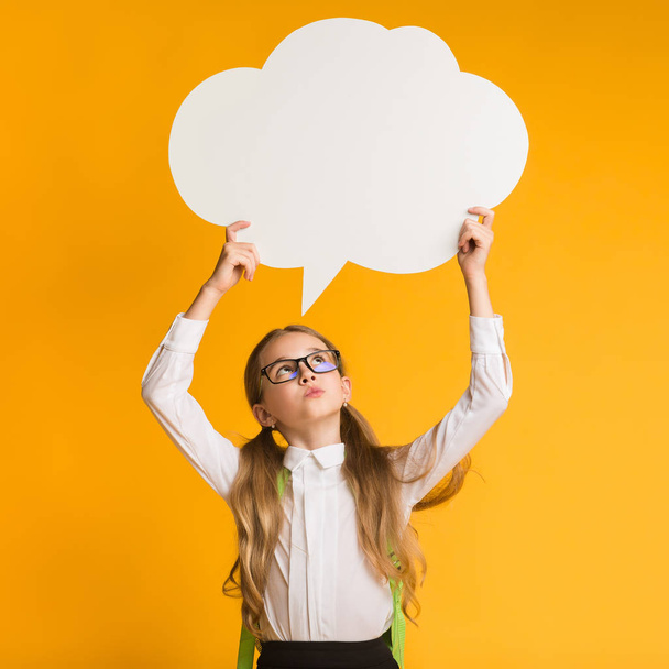 Pensive Elementary School Girl Holding Speech Bubble Overhead, Yellow Background - Photo, Image