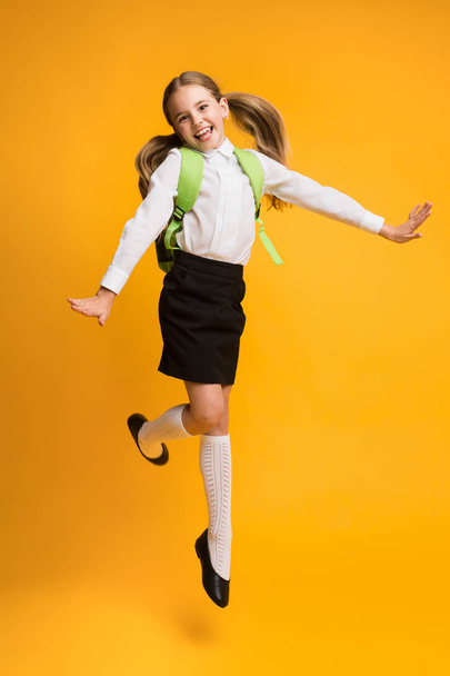 Excited Little Schoolgirl Jumping Over Yellow Studio Background. - Valokuva, kuva