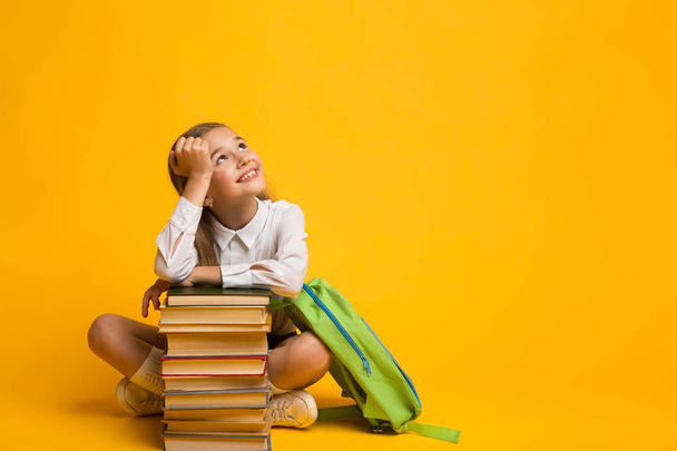 Cute Girl Dreaming About School Sitting With Backpack And Books - Foto, imagen