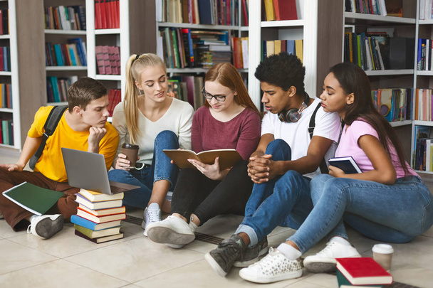 Grupo de estudantes diversos sentados no chão da biblioteca
 - Foto, Imagem