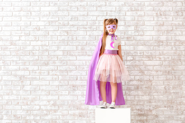 Χαριτωμένο κοριτσάκι ντυμένος ως υπερήρωας κοντά τούβλο τοίχο - Φωτογραφία, εικόνα
