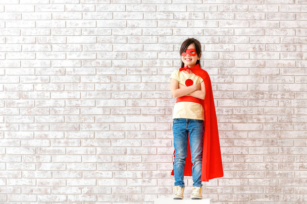 レンガの壁の近くにスーパーヒーローの服を着たかわいい女の子 - 写真・画像