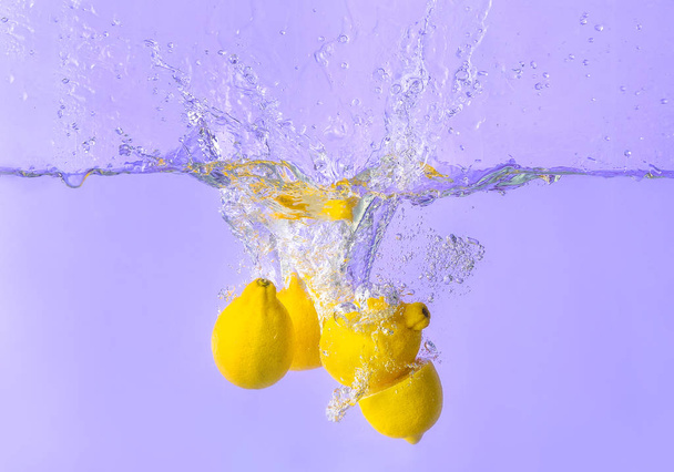 Vallen van citroenen in water op kleur achtergrond - Foto, afbeelding