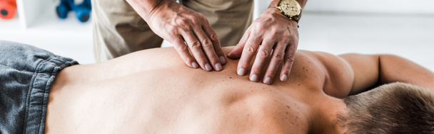 panoramische shot van chiropractor doen massage naar man op massagetafel  - Foto, afbeelding