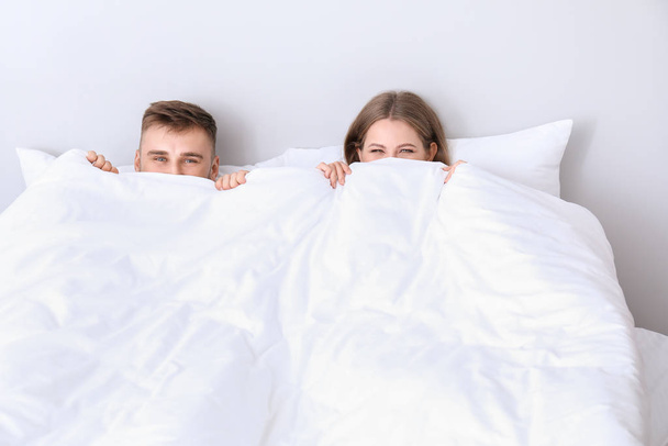Portrait de jeune couple caché sous la couverture dans la chambre
 - Photo, image