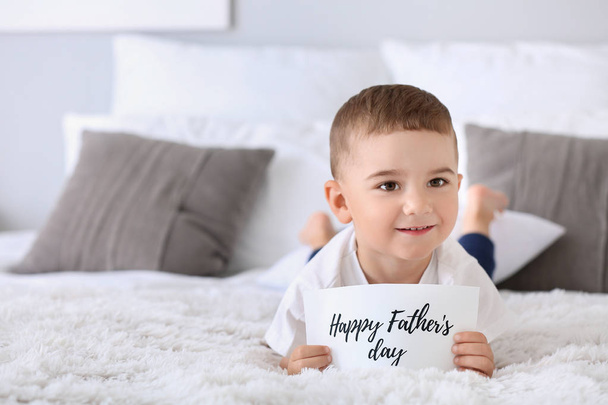 Cute little boy with greeting card for Father's Day lying on bed - Fotografie, Obrázek