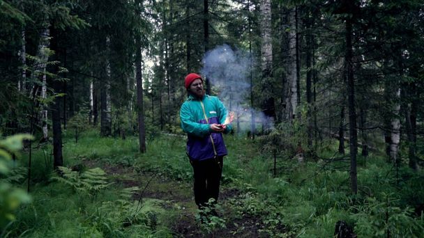 Man with colored smoke bombs in nature. Stock footage. Young man set fire to smoke bombs and they sparkled before smoke in forest - Photo, Image