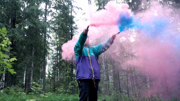 Hombre con bombas de humo de colores en la naturaleza. Imágenes de archivo. Joven hombre extiende corrientes de coloridas damas de humo en bosque denso
 - Foto, Imagen