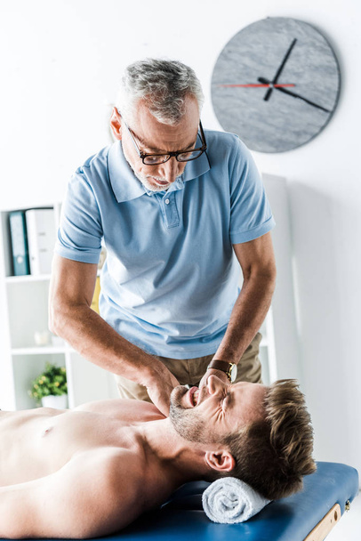  quiropráctico barbudo haciendo masaje al hombre con dolor en la mesa de masaje
  - Foto, Imagen