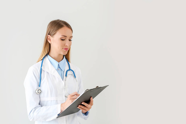 Female doctor with stethoscope and clipboard on light background - Photo, image