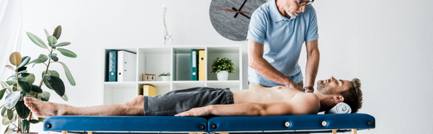 Panoramaaufnahme eines bärtigen Chiropraktikers, der einem Mann auf einem Massagetisch massiert  - Foto, Bild