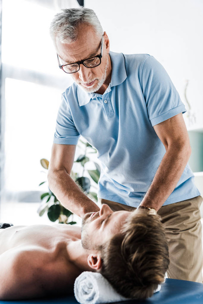 enfoque selectivo de quiropráctico barbudo haciendo masaje al hombre en la mesa de masaje
  - Foto, Imagen