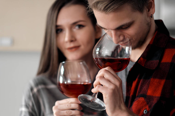 台所でチェック柄のシャツを着た美しい若いカップルが食べ物を準備し、メガネから赤ワインを飲む. - 写真・画像