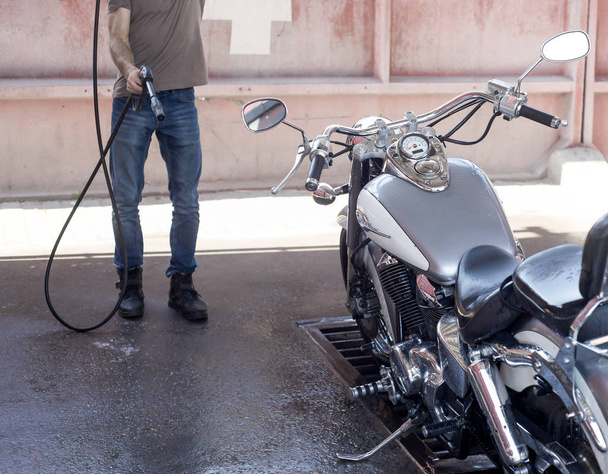 Mann wäscht Motorrad in der Waschanlage mit Wasser und Schaum.  - Foto, Bild