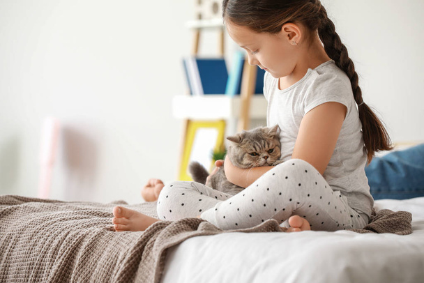 Маленька дівчинка з милою кішкою сидить на ліжку вдома
 - Фото, зображення