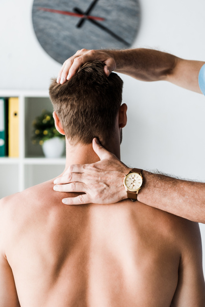 cropped view of doctor touching neck of muscular patient sitting in clinic  - Fotoğraf, Görsel