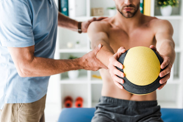 cropped view of doctor standing near patient working out with ball  - Fotoğraf, Görsel