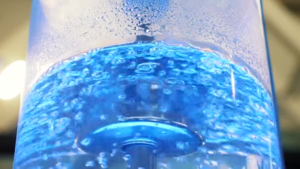 Forrásban lévő víz nagy üveghűtő a neon háttérvilágítás és fém cső. Média. Közelről kilátás-ból legtisztább víz-ban hűtőtáska-val buborék van megvilágít-val színdús könnyű - Felvétel, videó