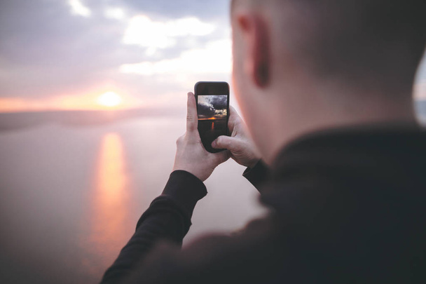 Hipster traveler taking photo on phone of amazing sunset view on - 写真・画像